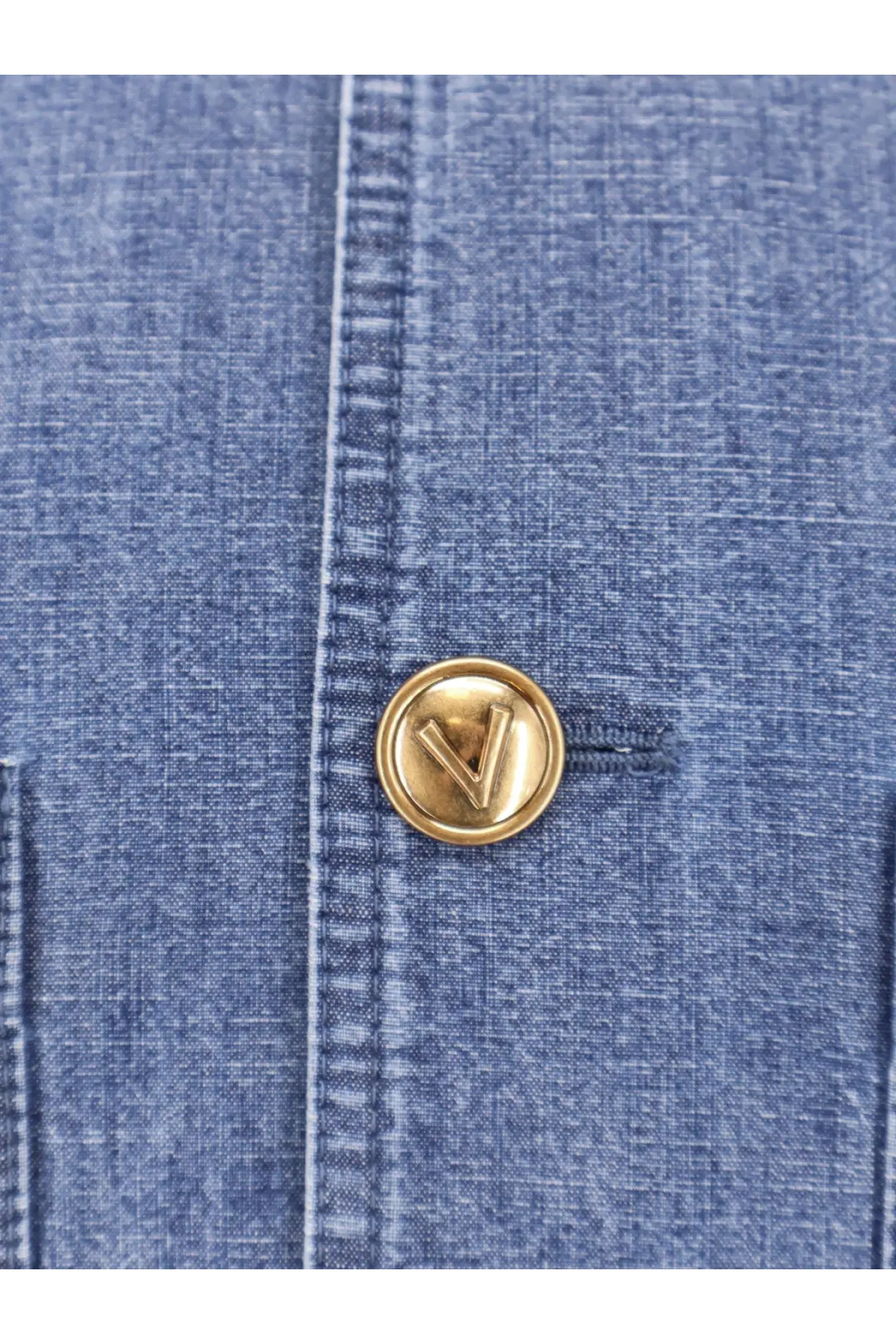 Gold-toned circular button with raised v logo on blue denim fabric of valentino men’s valentino denim sahariana jacket