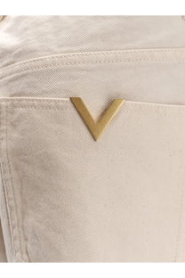 Valentino men’s white cotton trousers featuring a gold-tone v-shaped metal logo pin on off-white denim fabric