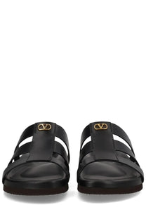 Valentino men’s Sandalo slide sandals in black leather with gold-tone v-logo hardware and studshield detail