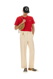 A tan leather crossbody bag with gold-tone hardware and chain strap shown alongside a Valentino men’s red shirt