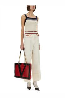 Red and black Valentino tote bag with gold chain handles paired with Valentino women’s white crepe couture pants