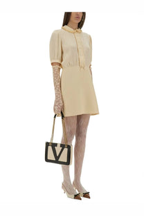 Black and cream leather handbag with gold-tone chain strap and bold monogram logo paired with valentino white crepe dress