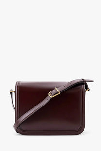 A sleek dark burgundy leather shoulder bag with gold-tone buckle and adjustable strap by Valentino Garavani