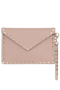 A blush pink leather envelope clutch adorned with gold-tone pyramid studs along its edges and a matching wrist strap.