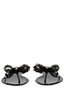 Valentino women’s black glossy flip-flops with gold-tone pyramid studs on a bow-adorned strap