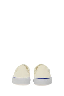Vans unisex slip-on sneaker reissue in cream canvas with white rubber sole and thin purple stripe along the edge