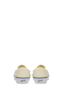 Back view of cream-colored canvas vans unisex slip-on sneaker with blue stripe and white rubber outsole showing vans logo