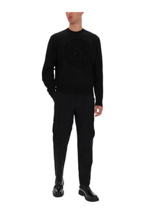 Black knit sweater by Versace Jeans Couture with raised circular logo on chest in jersey material