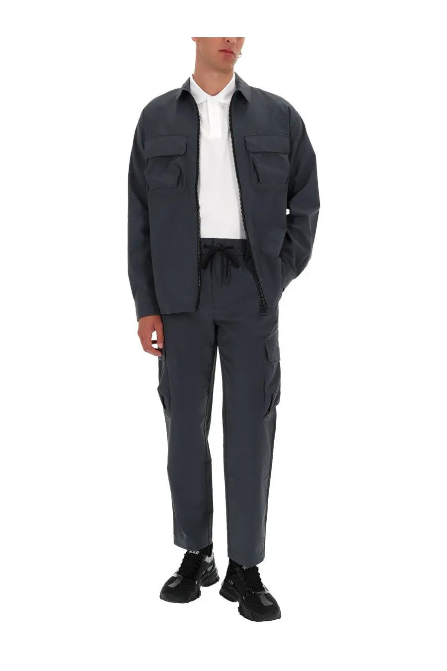 Dark gray utility jacket with two chest pockets and front zipper worn over white polo with versace jeans couture grey cargo pants