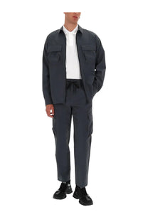 Dark gray utility jacket with two chest pockets and front zipper worn over white polo with versace jeans couture grey cargo pants