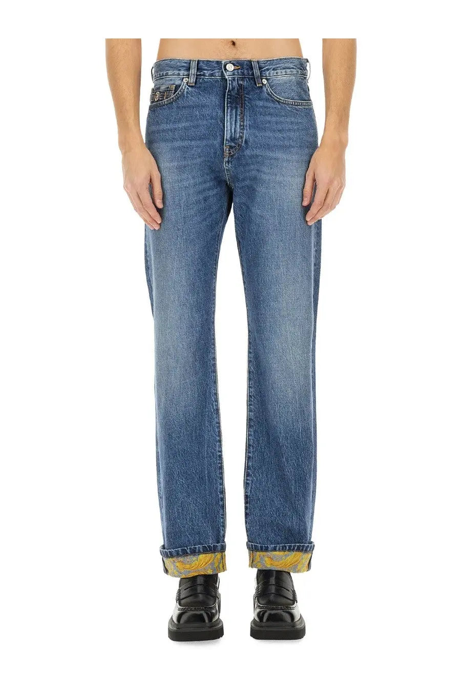 Versace men’s jeans in denim blue with faded wash and rolled cuffs showing yellow patterned lining