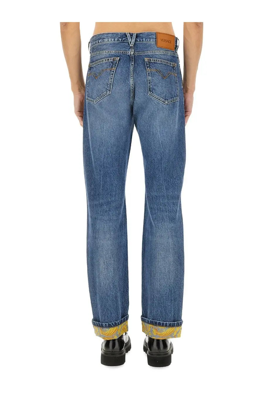 Versace men’s blue denim jeans with faded wash rolled cuffs showing yellow patterned lining and leather brand patch