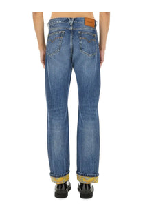 Versace men’s blue denim jeans with faded wash rolled cuffs showing yellow patterned lining and leather brand patch