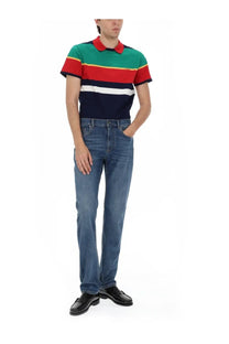 A man wearing a colorful striped polo shirt with red green navy blue and white bands paired with versace denim jeans