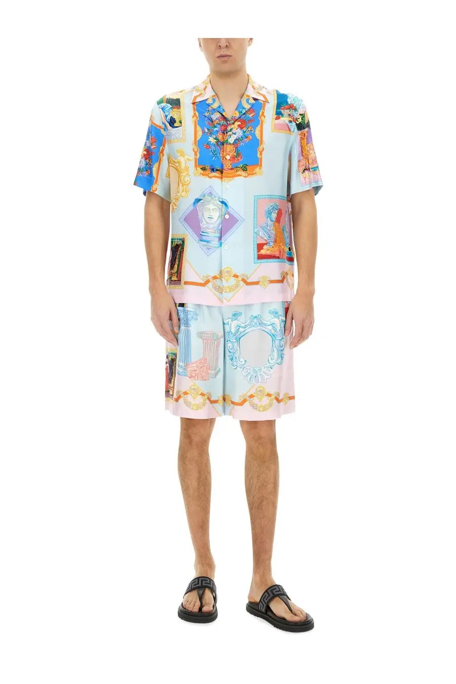 A man wearing versace men’s silk shorts and a matching short-sleeved shirt with ornate multicolor classical motifs on light blue fabric