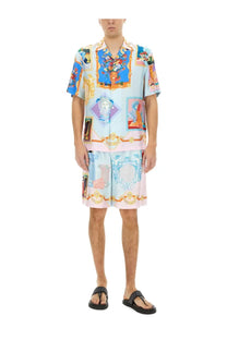 A man wearing versace men’s silk shorts and a matching short-sleeved shirt with ornate multicolor classical motifs on light blue fabric