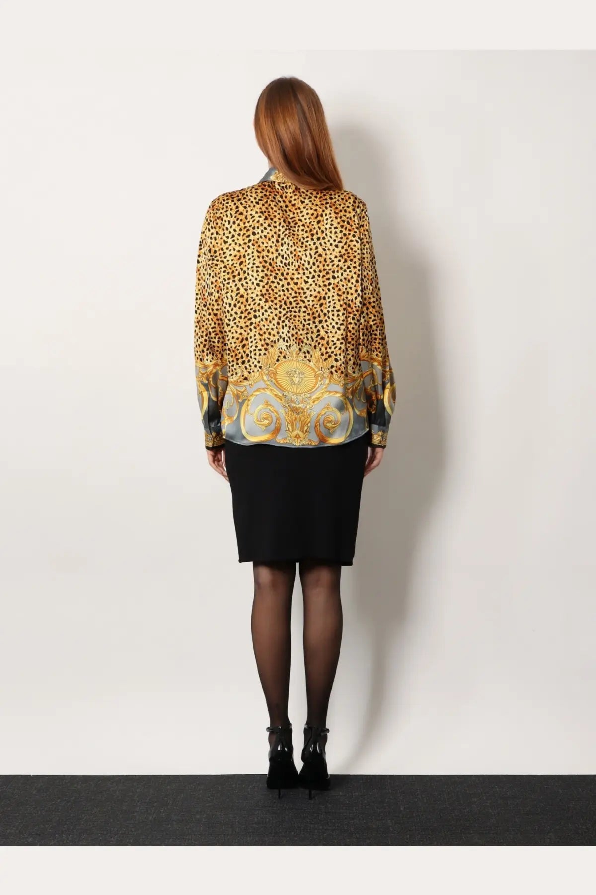 A woman wears a grey Versace women’s cheetah foulard lavallière silk shirt with sheer long sleeves and gold hem detailing