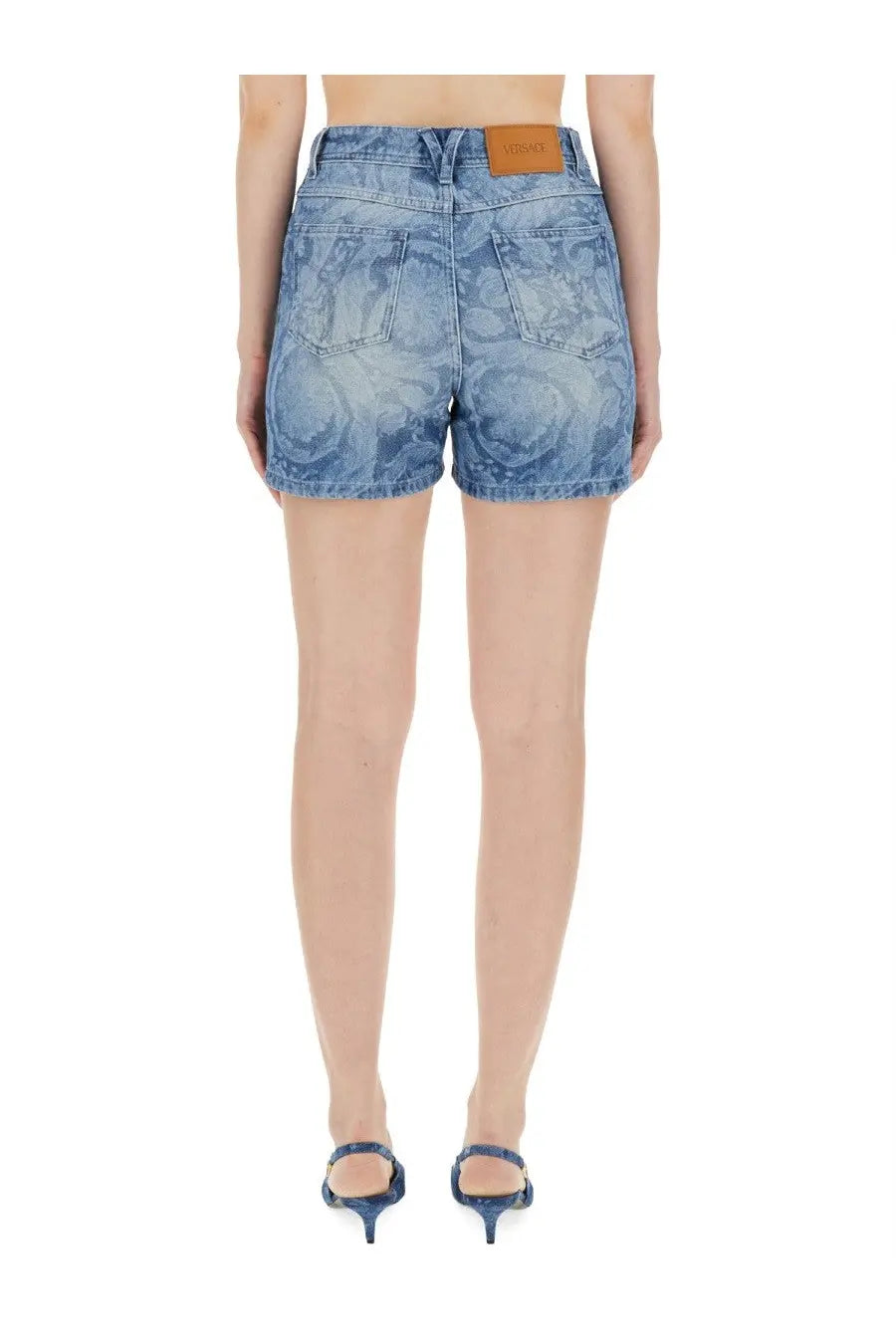 Versace women’s blue denim shorts with a faded swirling pattern and brown leather brand patch at the waistband