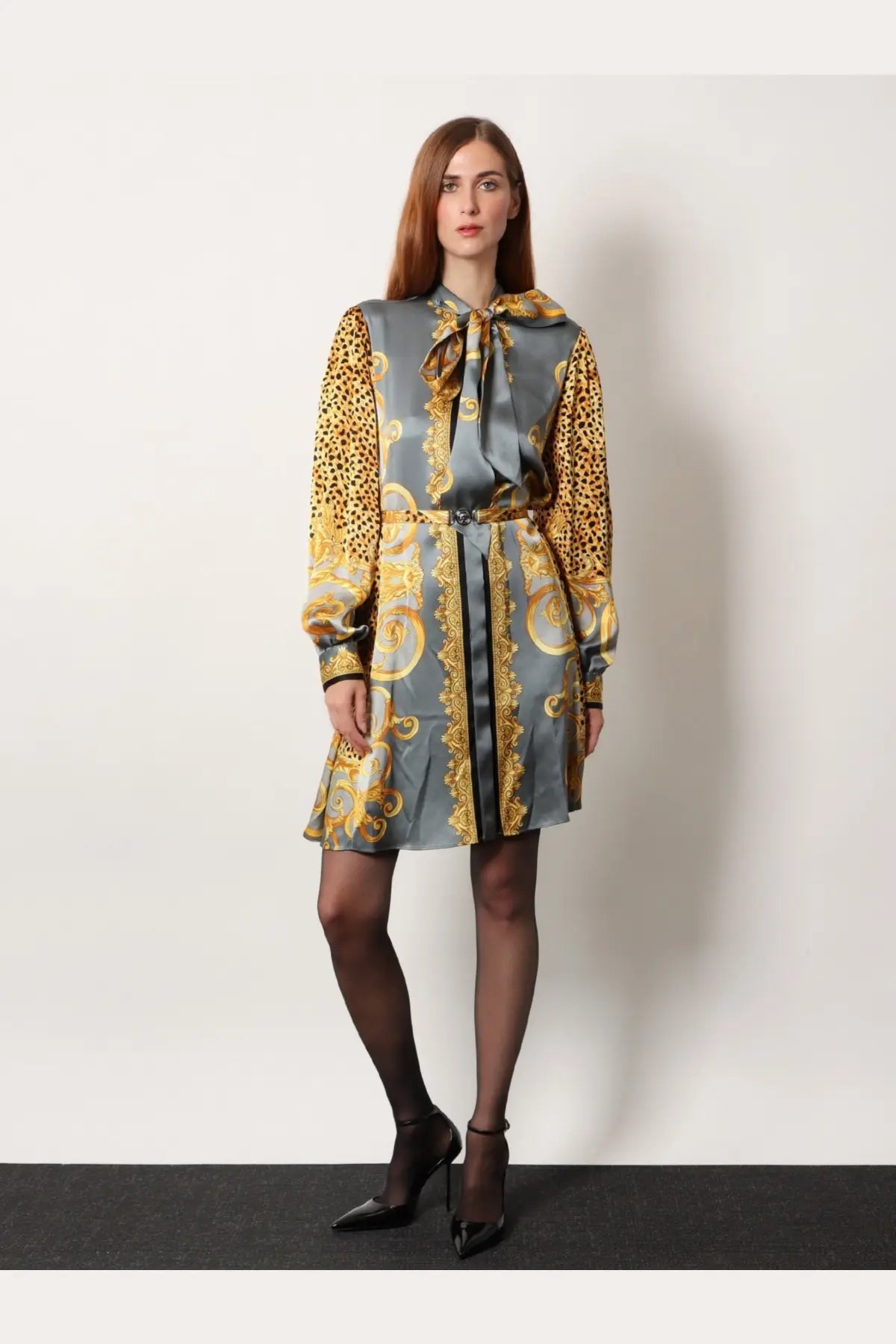 A woman wears a versace women’s silk chemisier dress grey with gray and gold pattern and leopard print sleeves with bow neckline