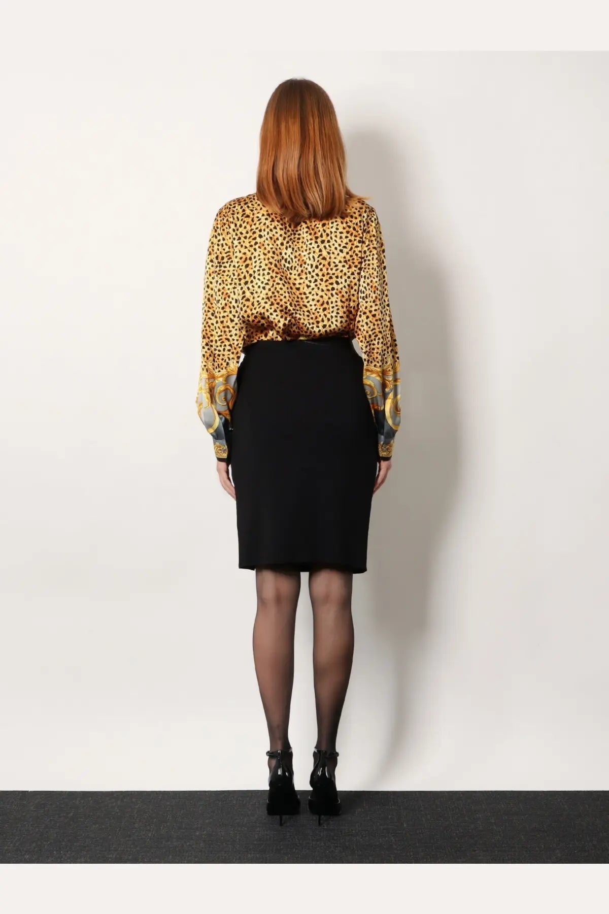 A woman wearing a versace women’s black stretch viscose midi skirt paired with a gold and black leopard-print blouse