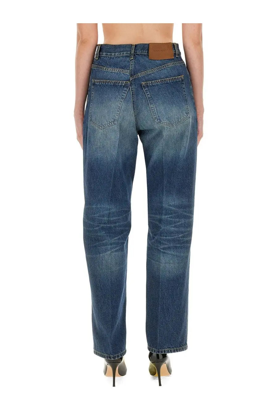 Back side of victoria beckham women’s boyfriend jeans in medium blue denim with subtle fading and brown leather patch