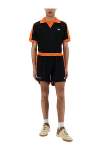 Wales Bonner men’s jersey shorts in black shown with a black and orange short-sleeved polo shirt with contrasting trim