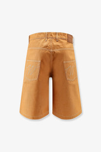 Back view of walk in paris men’s baggy orange denim shorts in tan cotton with white embroidered logos and brown leather patch