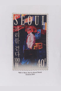 A rectangular postage stamp showing a man in sunglasses next to crates with seoul text, walk in paris men’s white cotton shirt