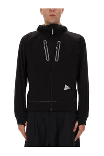 Black hooded jacket with reflective silver zippers and a triangular logo patch by and wander men’s alpha air jacket black