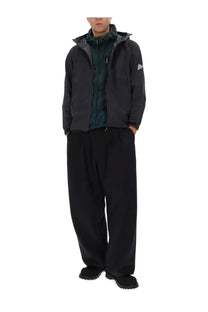 And wander men’s grey dark gray hooded jacket with subtle triangular logo on sleeve worn over dark green patterned shirt