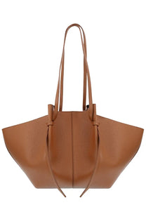 Tan leather tote bag with structured slightly flared silhouette and dual top handles tied at front by yuzefi