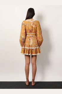 A woman wears a Zimmermann women’s frill cotton short dress in yellow with floral print lace trim and long puffed sleeves