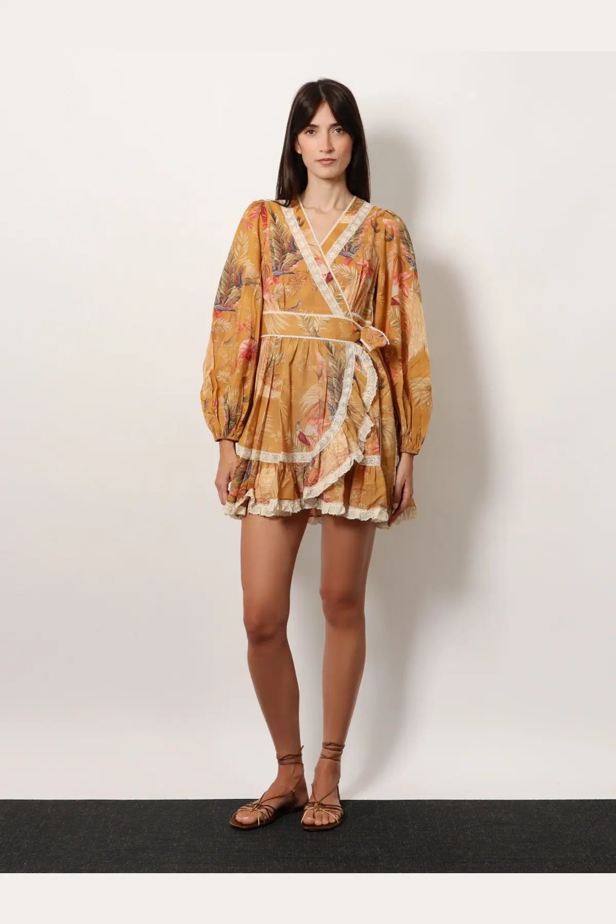 A woman wears a mustard-yellow Zimmermann women’s frill cotton short dress with floral print lace trim and puffed sleeves
