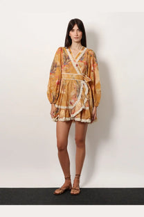 A woman wears a mustard-yellow Zimmermann women’s frill cotton short dress with floral print lace trim and puffed sleeves