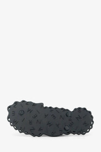 Black glossy plastic hair clip with scalloped edge and embossed lettering shown with zimmermann seafoam thong sandals