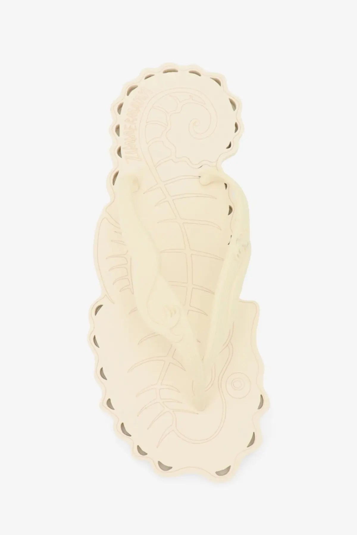 Cream-colored rubber flip-flop-shaped coaster with intricate cut-outs scalloped edge and embossed pattern for table use